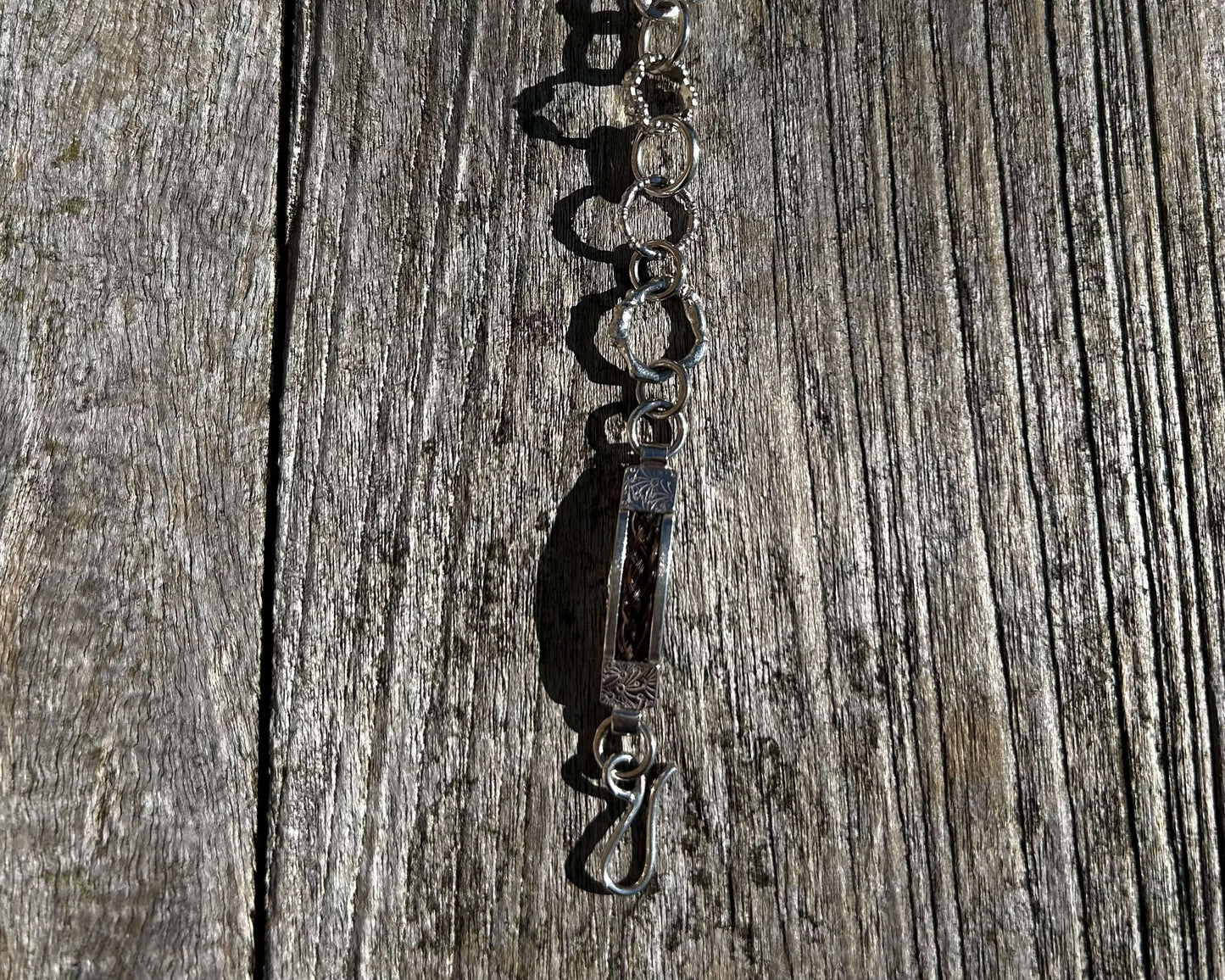 Close-up of a handcrafted sterling silver horse hair charm bracelet on a wooden surface.