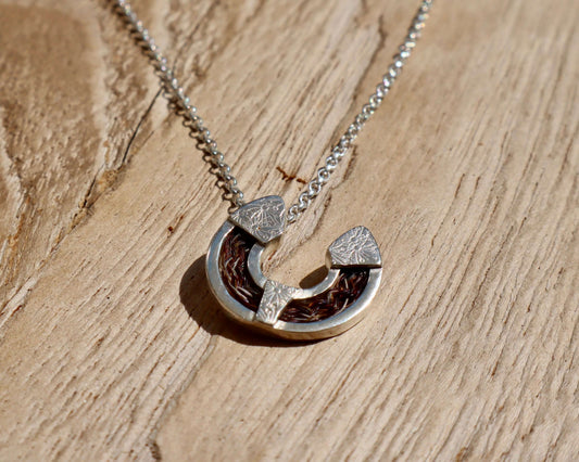 Horse hair horseshoe necklace featuring handcrafted sterling silver pendant with braided tail hair, on a silver chain.